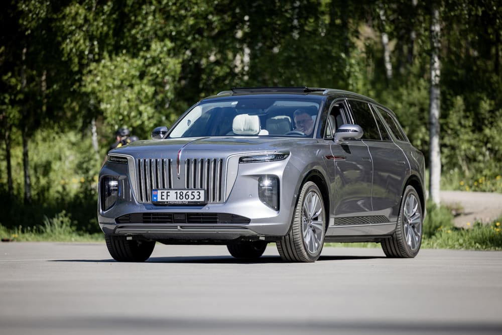 Grå Hongqi E-HS9 foran grønne trær og busker